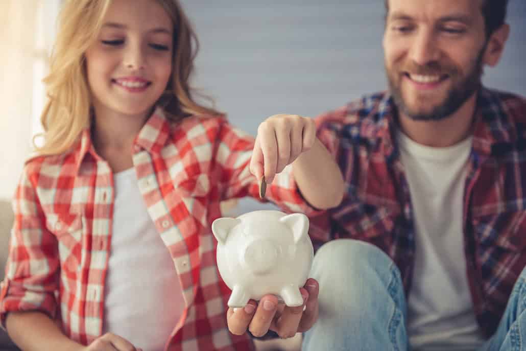 Girl putting money into piggy bank held by dad