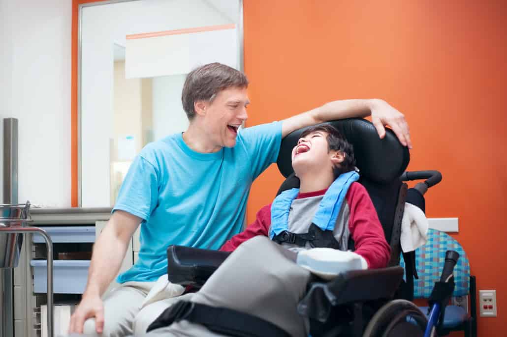 A man with a child laughing in a wheelchair