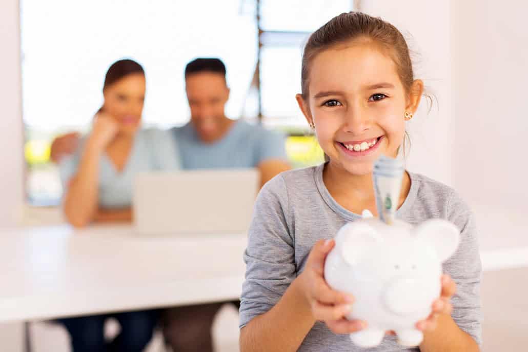 Girl holding a piggy bank with parents in the background