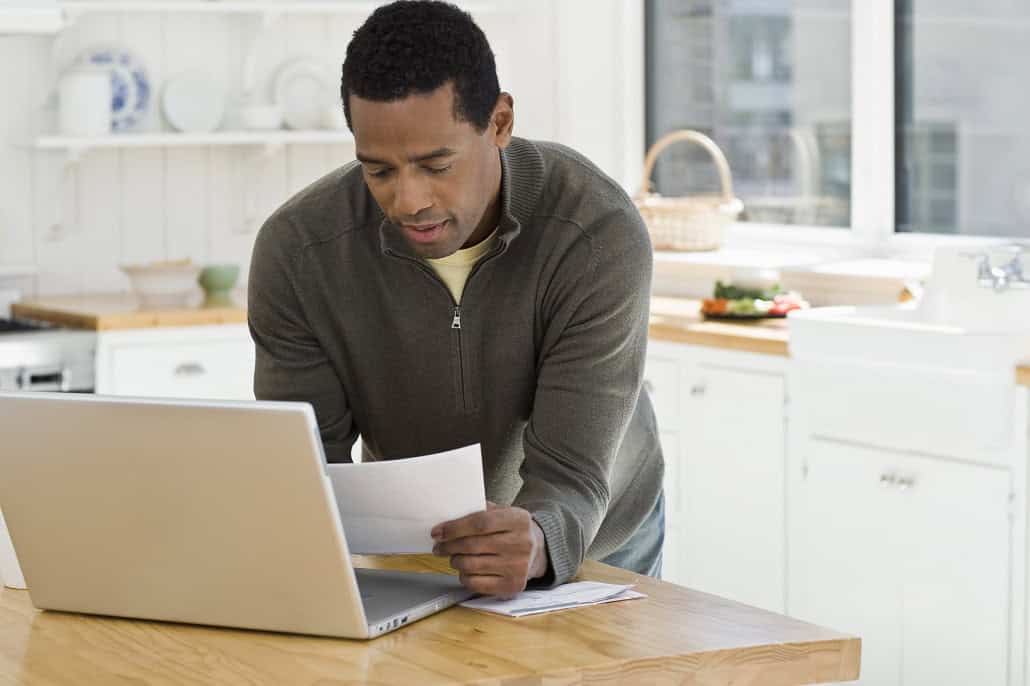 Man looking at student loan paperwork in front of laptop