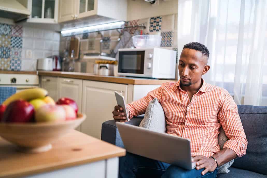 Man using phone and laptop to learn about income-driven loan repayment