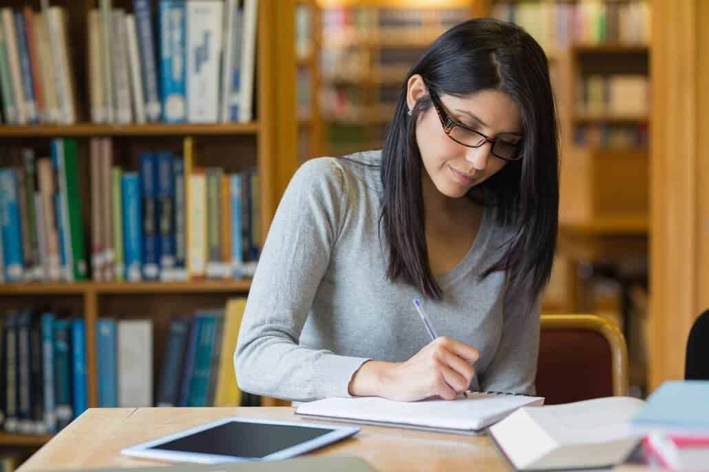 Girl working in the library with books and a tablet